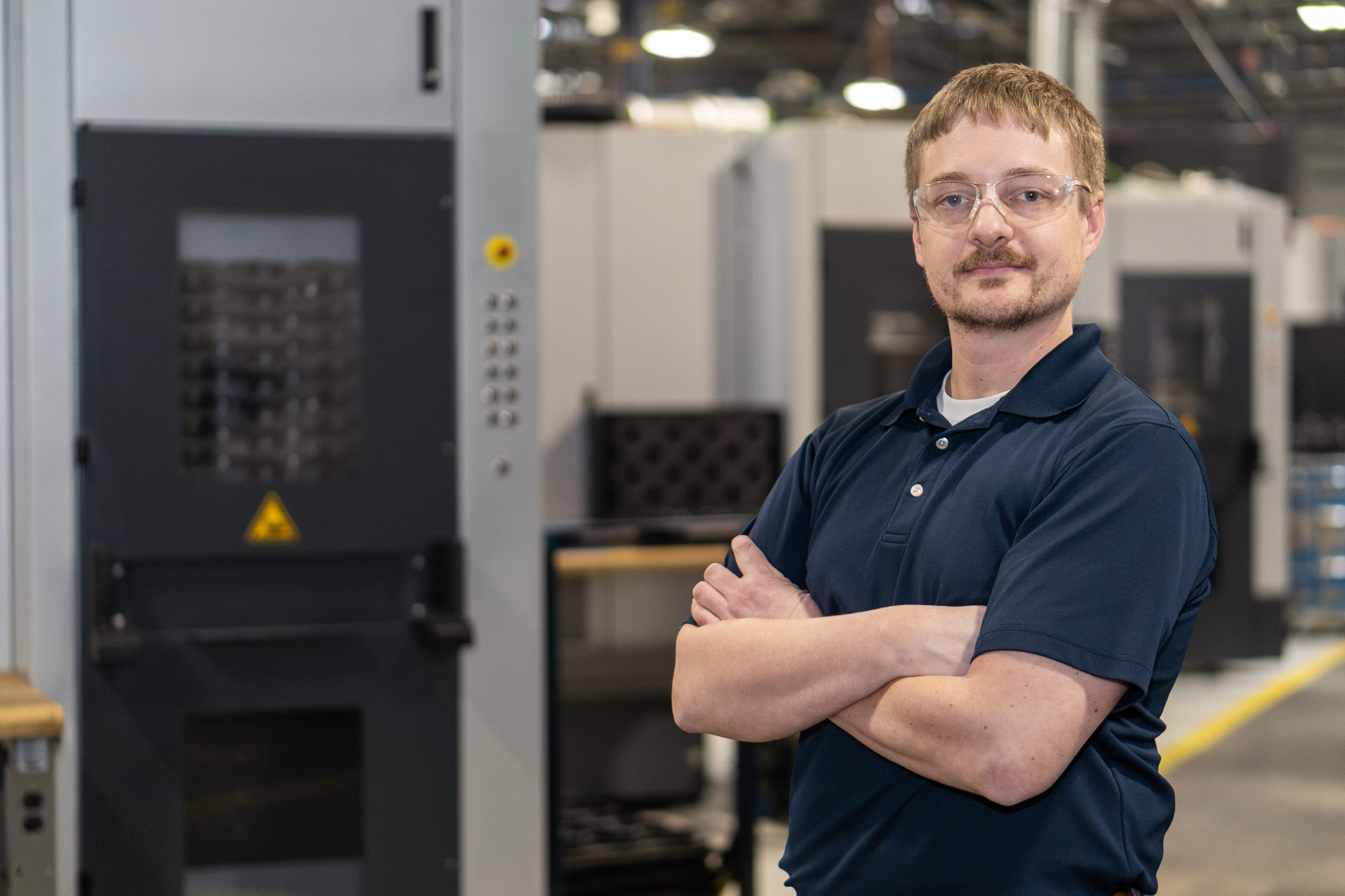 A young white man with red hair and glasses stands with his arms crossed.