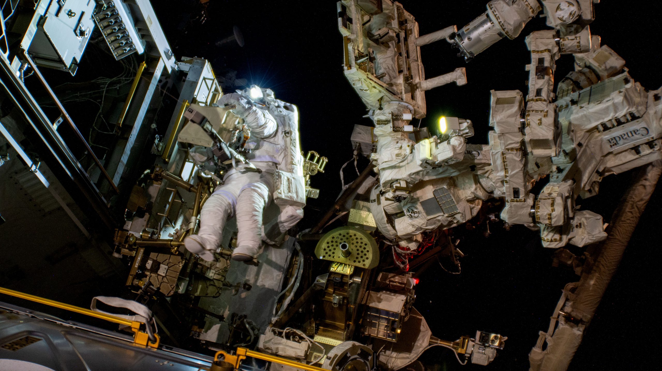 Astronaut Suni Williams (just left of center) wears a white spacesuit while she conducts a spacewalk outside of the International Space Station.
