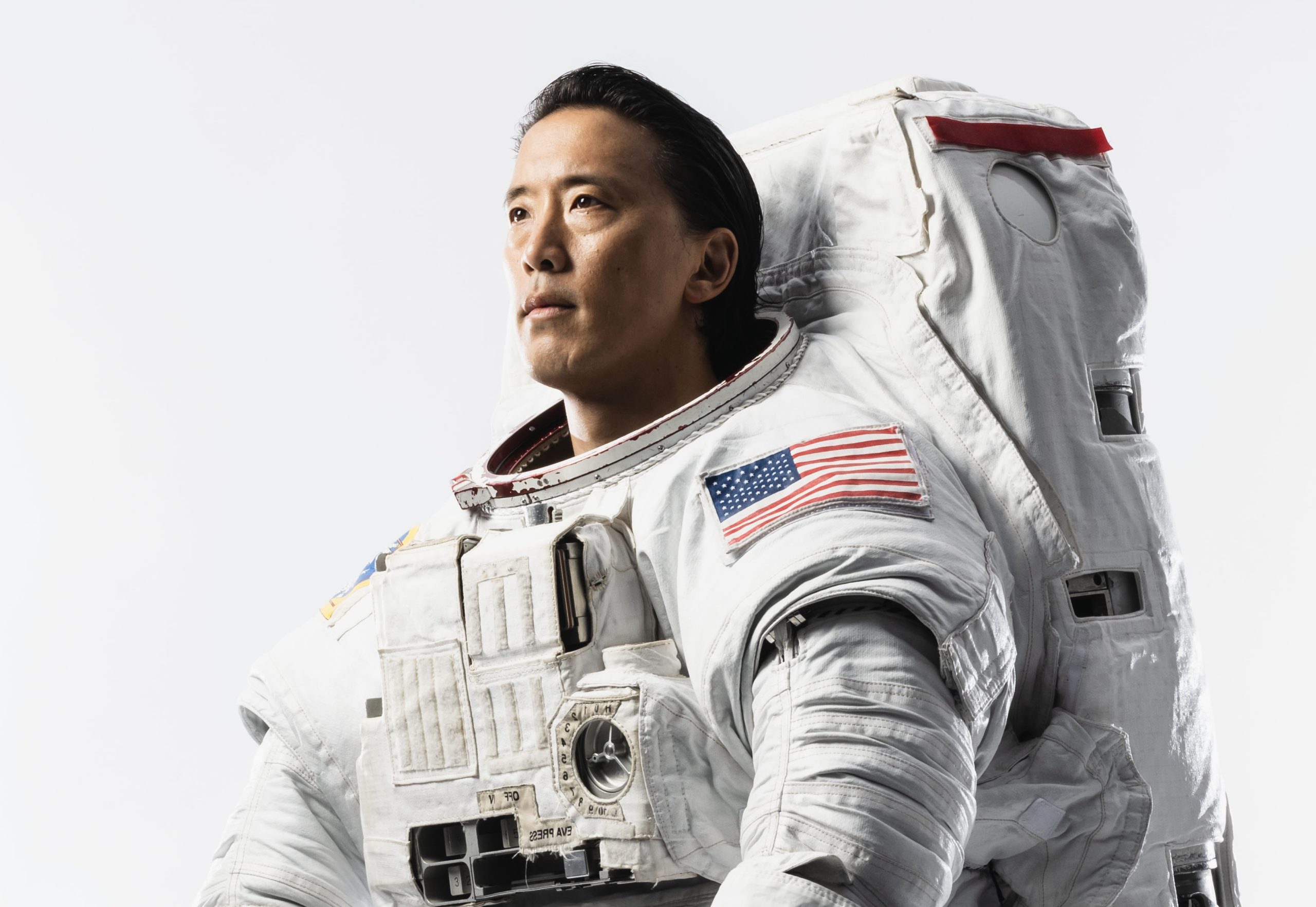 NASA astronaut Jonny Kim looks off-camera, dressed in a white space suit with an American flag on the sleeve.
