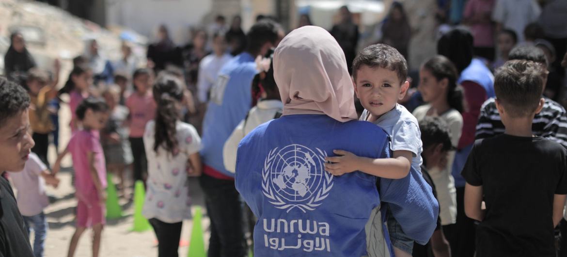 An UNRWA worker carries a young boy in Gaza. An UNRWA worker carries a young boy in Gaza.