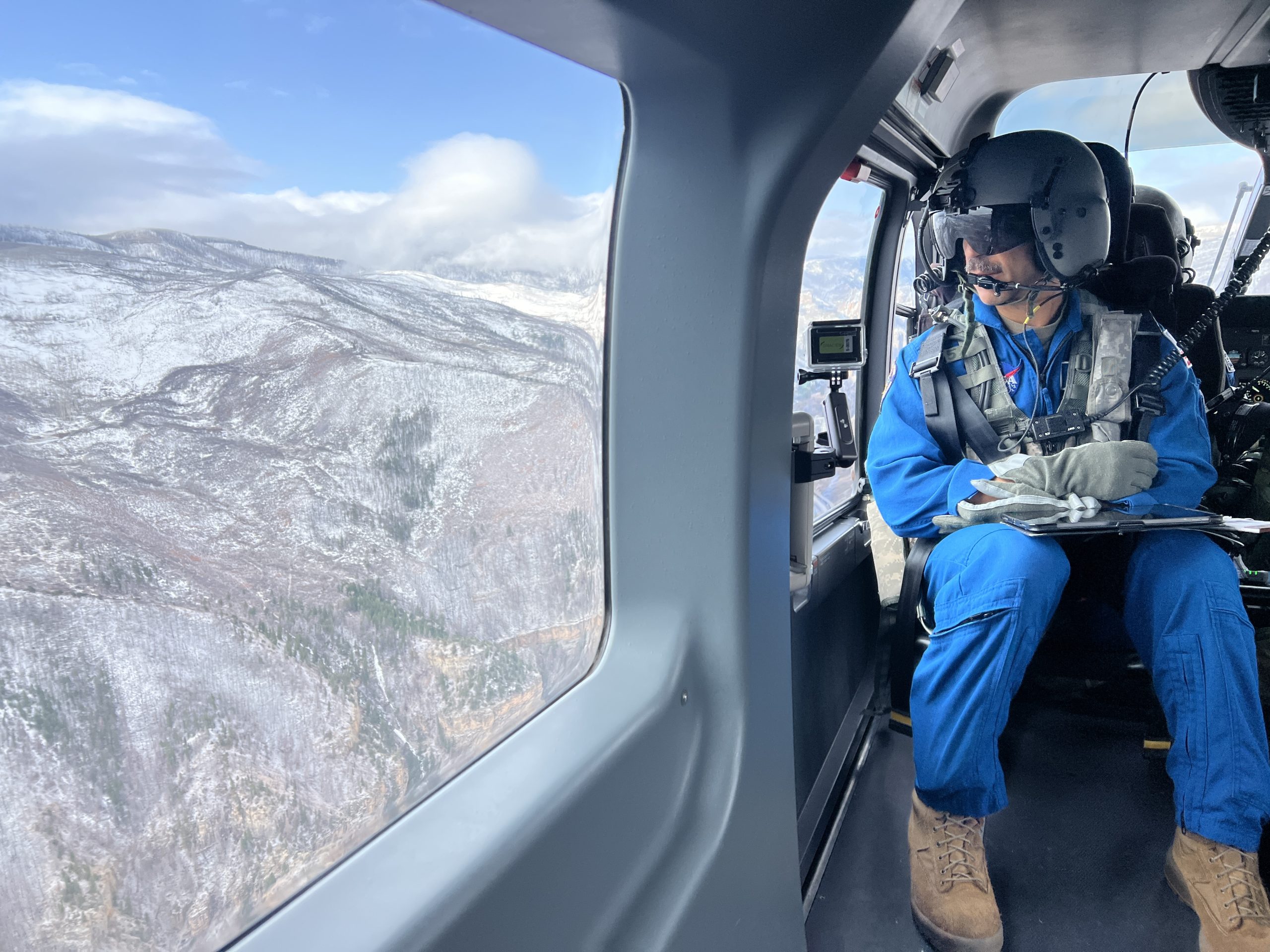 An astronaut in a helicopter looks out the window in their