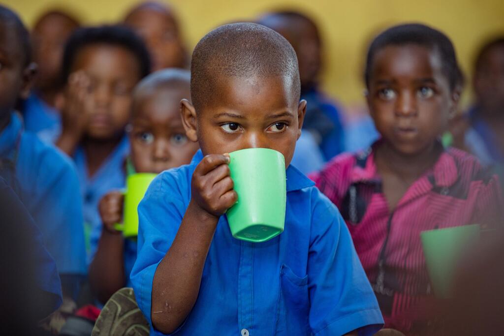 A young child attends school in Burera District, Rwanda. A young child in a blue shirt drinks from a green cup in a classroom setting, surrounded by other children. This image captures a moment from a UNICEF-supported early childhood development initiative in Burera District, Rwanda.