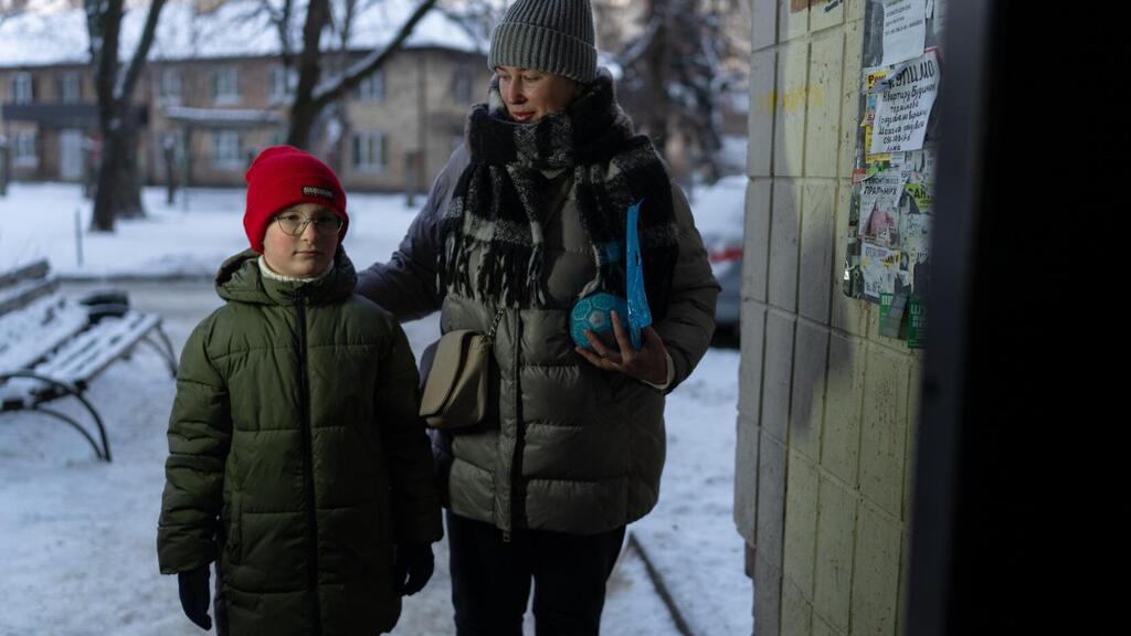 A woman and child in winter attire stand outside in a snowy urban area in Ukraine. A woman and a child dressed in winter clothing stand outside a building in a snowy urban setting in Ukraine.