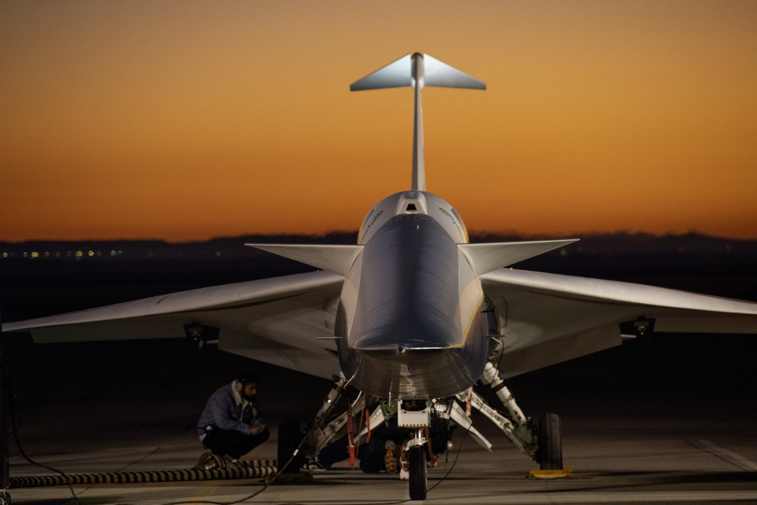 An aircraft resting on a section of runway as seen from the front, with its nose facing the camera. The early morning sky is orange in the background.