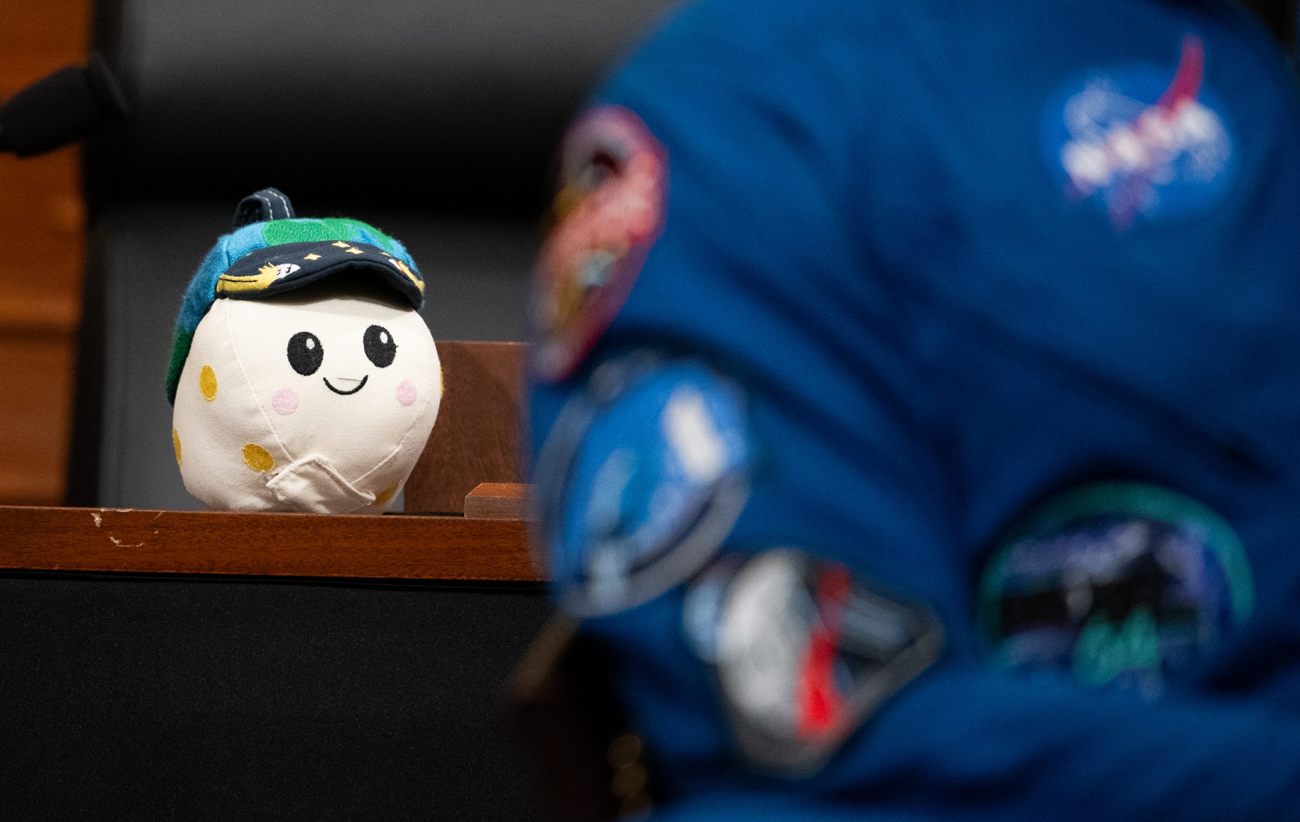 Rise, the Artemis II zero gravity indicator, sits on a wooden desk. A NASA astronaut is in the foreground.